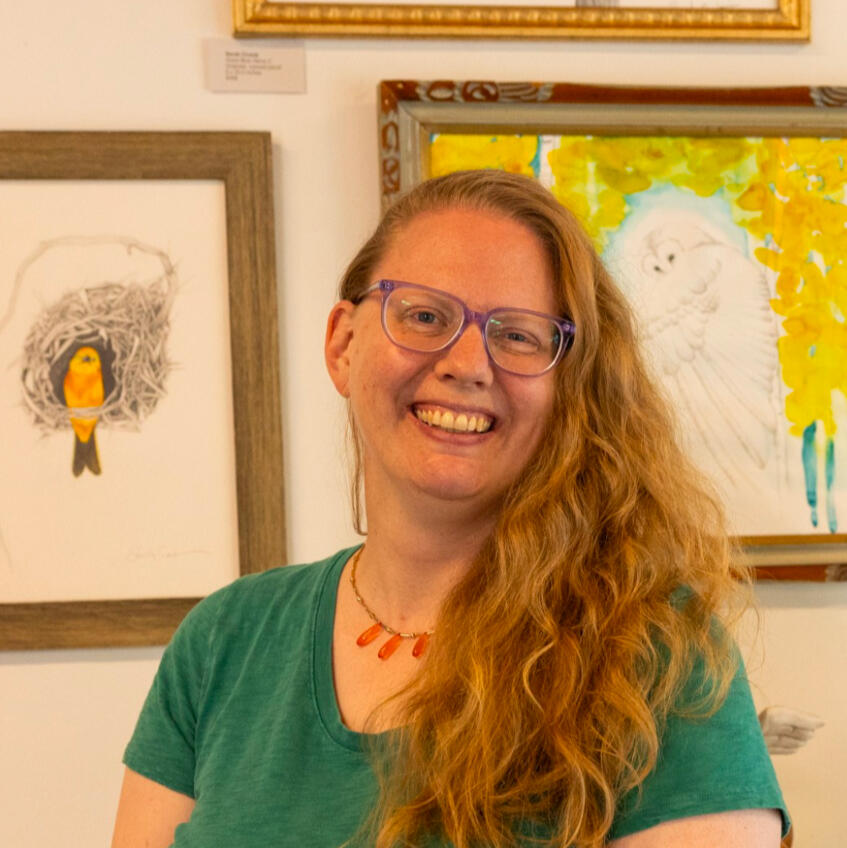 Adult blonde lady smiling in front of silver art on a wall.
